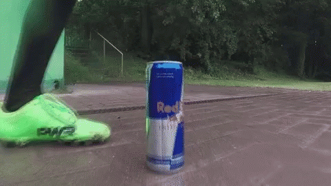 Person Kicking Red Bull Can on Sidewalk