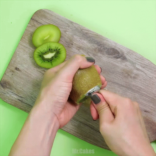 Person Peeling Kiwi on Wooden Board With Mr.Cakes