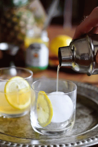 Person Pouring Drink Into Glass With Ice And Lemon GIF