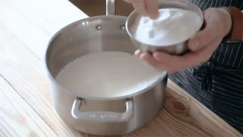 Person Pouring Sugar Into Pot of Milk