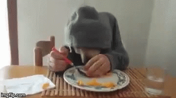 Person Sitting at Table Eating With Fork and Spoon