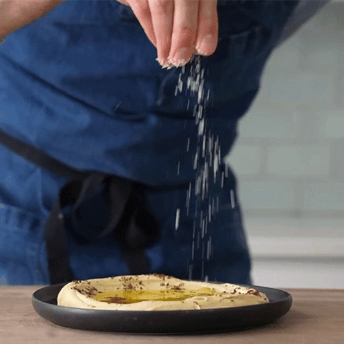 Person Sprinkling Salt on Hummus