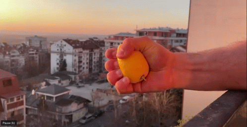 Person Squeezing Orange With City Pause (N) GIF