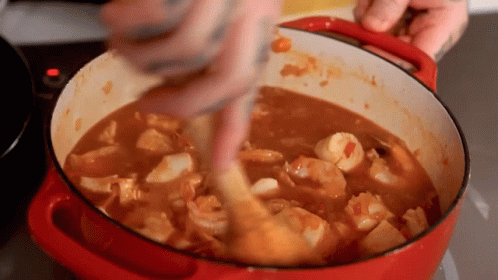Person Stirring Pot of Shrimp Stew With Wooden Spoon