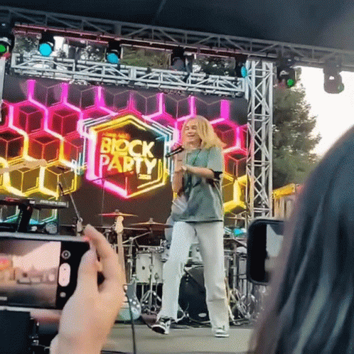 Person Taking Picture of Girl on Stage With Block Party Sign