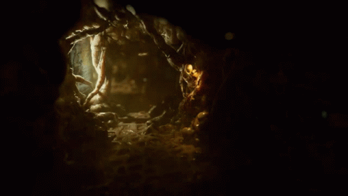 Person Walking in Dark Cave With Green Light on Chest