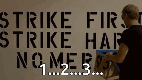 Person Working On Wall Saying Strike First Strike Hard No Mercy GIF