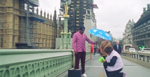 Pink-Suited Man Holds Blue Umbrella Over Woman Bridge GIF