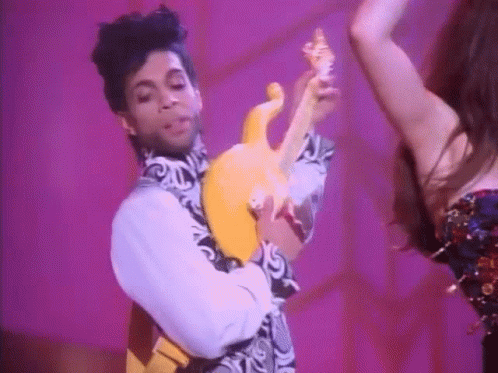 Prince Is Holding A Yellow Guitar While Dancing With A Woman Behind Him . GIF