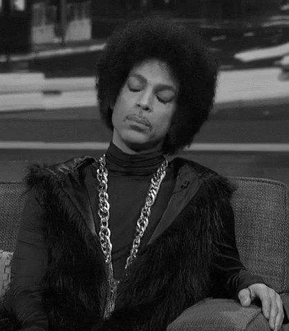Prince Is Sitting On A Couch Wearing A Fur Vest And A Chain . GIF