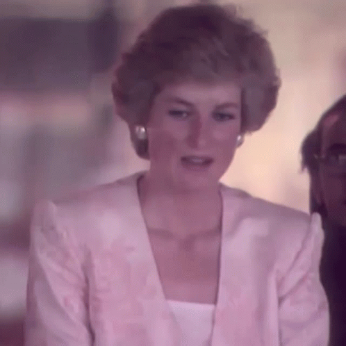 Princess Diana Is Wearing A Pink Jacket And White Top While Sitting In Front Of A Man . GIF