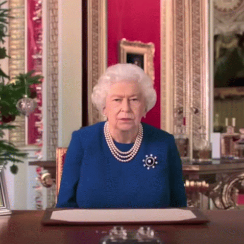 Queen Elizabeth Wearing A Blue Dress And Pearls Sits At A Table GIF