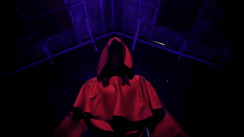 Red Hooded Person Arms Outstretched in Dark Room