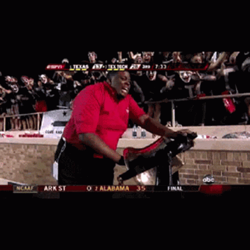 Red Shirt Man Riding Exercise Bike with Masked Crowd