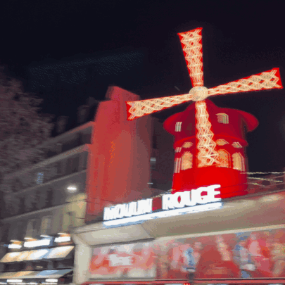 Red Windmill Lit Up In Front Of Moulin Rouge Sign GIF