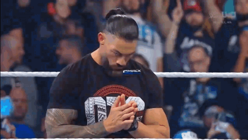 Roman Reigns Is Standing In A Wrestling Ring With His Hands Folded In Front Of A Crowd . GIF