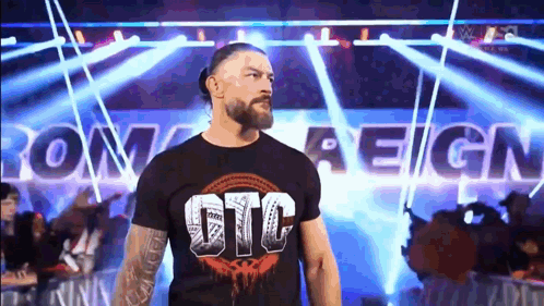 Roman Reigns Is Walking Out Of The Ring Wearing A Black T-Shirt With The Word Reign On It . GIF
