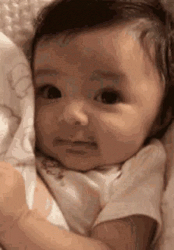 Sad Baby Lying In Blanket Looking At Camera GIF