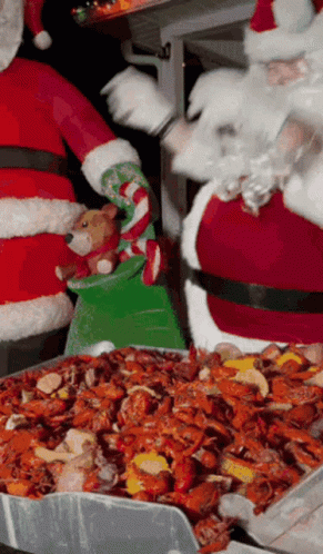Santa Claus Is Holding A Stuffed Animal While Standing Next To A Tray Of Crawfish GIF