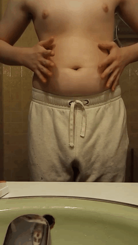 Shirtless Man Holding Belly at Bathroom Sink