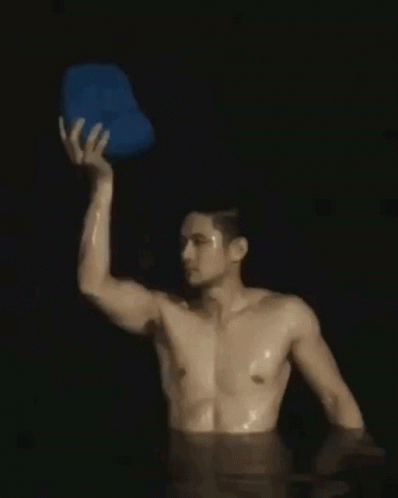 Shirtless Man Holding Blue Bucket Over Head in Water