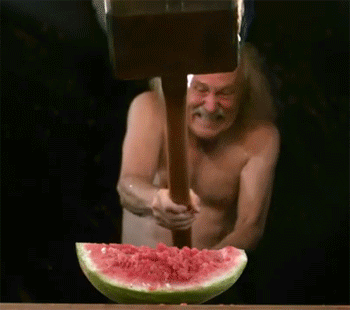 Shirtless Man Holding Wooden Hammer Over Watermelon GIF