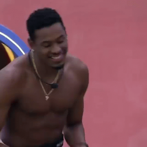 Shirtless Man in Necklace Smiling on Red Surface