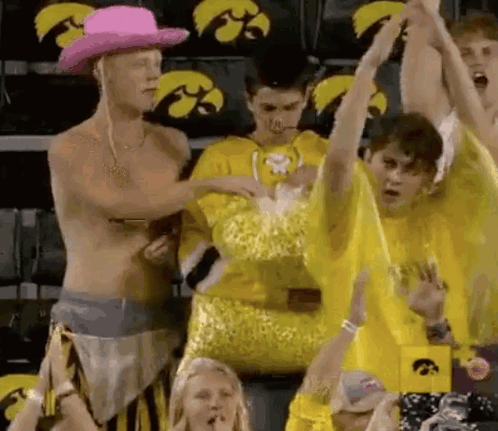 Shirtless Man in Pink Cowboy Hat in Front of Yellow Shirt Crowd