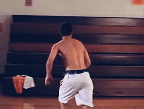 Shirtless Man in White Shorts in Front of Bleacher