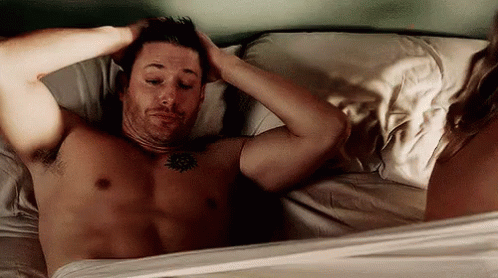 Shirtless Man Laying In Bed With Woman Standing Next To Him GIF