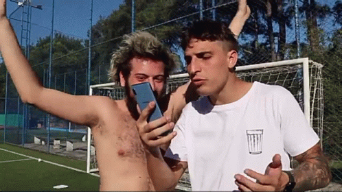 Shirtless Man Photographing Another Shirtless Man with Trash Can