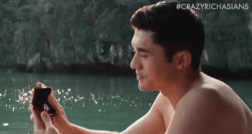 Shirtless Man Sitting in Water Holding Box With Ring