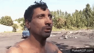 Shirtless Man Standing In Field With Blue Truck GIF