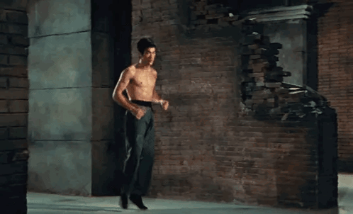 Shirtless Man Standing In Front Of Brick Wall GIF