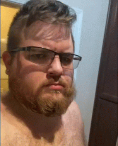 Shirtless Man With Beard and Glasses Taking Selfie in Bathroom