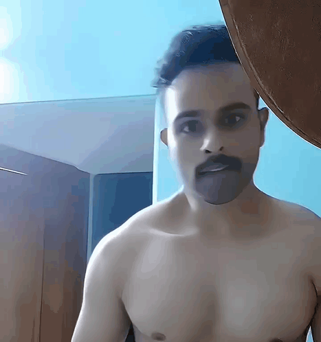 Shirtless Man With Mustache Standing in Front of Blue Wall
