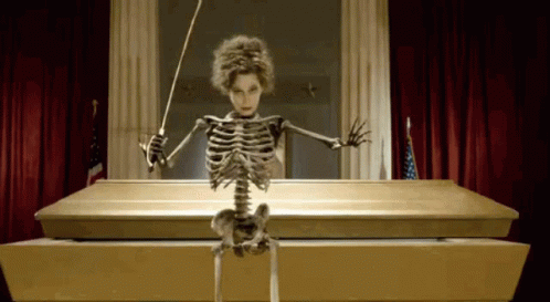 Skeleton Sitting in Coffin Holding Baton