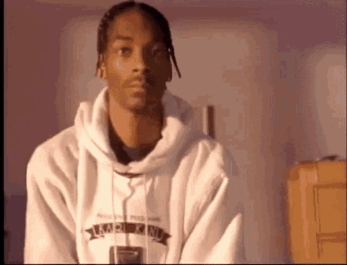 Snoop Dogg Is Wearing A White Hoodie And Looking At The Camera While Sitting In A Room . GIF