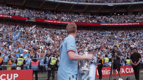 Soccer Player Holding Trophy in Crowd with Emirates