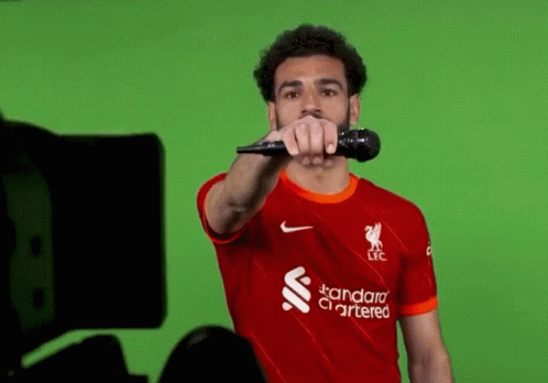 Soccer Player In Red Shirt Holding Microphone Pointing At Camera GIF