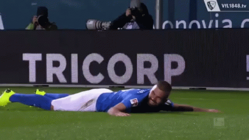 Soccer Player Laying on Field in Front of Tricorp Banner