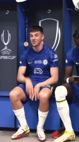 Soccer Player Sitting on Bench in Locker Room in Front of UEFA Super Cup Sign