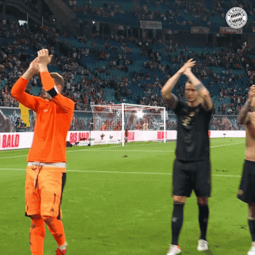soccer players applauding on a field with a big bald ad behind them