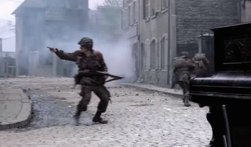 Soldiers Are Walking Down A Cobblestone Street With Smoke Coming From The Buildings GIF