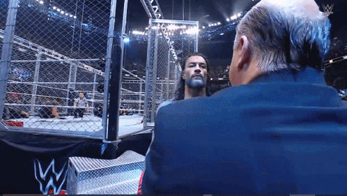 Suited Man Talking In Wrestling Ring W Logo GIF