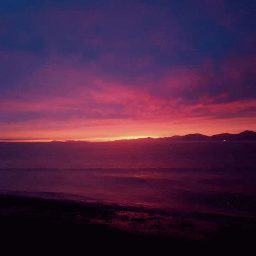 Sunset Over The Ocean With Mountains In The Background GIF