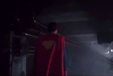 Superman Is Walking Through A Dark Room With A Red Cape On . GIF
