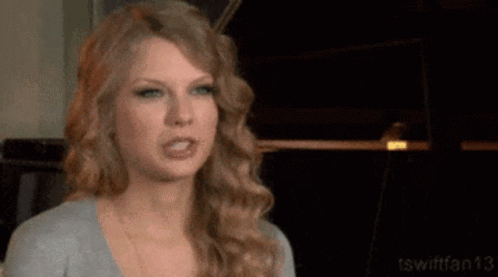 Taylor Swift Is Making A Funny Face While Wearing A Gray Shirt . GIF
