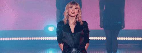 Taylor Swift Is Standing On A Stage In Front Of A Pink Background . GIF