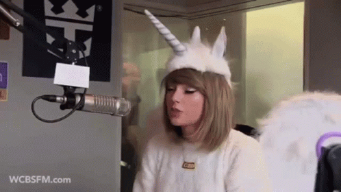 Taylor Swift Unicorn Hat and Wings Talking Into Microphone